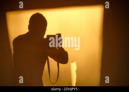 Autoportrait d'un photographe ombre sur un papier peint blanc dans la lumière jaune chaude du matin. Vu en Allemagne en novembre. Banque D'Images