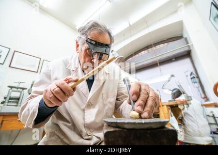 Faible angle d'un maître masculin mature et spécialisé orienté dans les verres utiliser un marteau et un burin tout en travaillant avec la pierre précieuse dans les bijoux atelier Banque D'Images