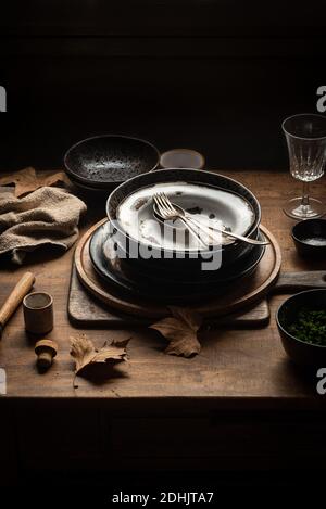 Grand angle de pile de plaques métalliques anciennes placées sur une table en bois avec divers ustensiles dans une maison de campagne sombre Banque D'Images