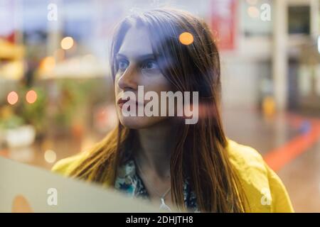 À travers un verre de jeune positif long cheveux de la femme regardant faites des emplettes dans une rue urbaine floue Banque D'Images