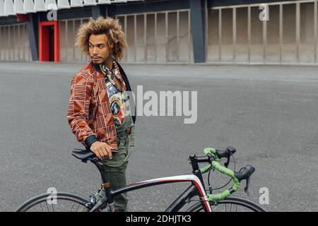 Un jeune boxer puit au poil de l'Afro-américain dans un vêtement tendance debout avec un vélo sur la place de la ville contre un bâtiment moderne loin Banque D'Images