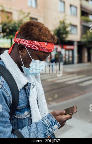 Vue latérale du jeune boxeur afro-américain en denim veste et bandeau avec masque médical jetable pour la prévention des coronavirus vérification du message Banque D'Images