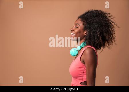 Rire jeune femme cubaine avec une coiffure afro portant une robe colorée et des écouteurs debout en studio Banque D'Images