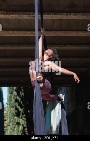 Angle bas de la flexible afro-américaine fait le yoga dans les airs se taillent tout en effectuant des fractionnements au-dessus du sol en ville Banque D'Images