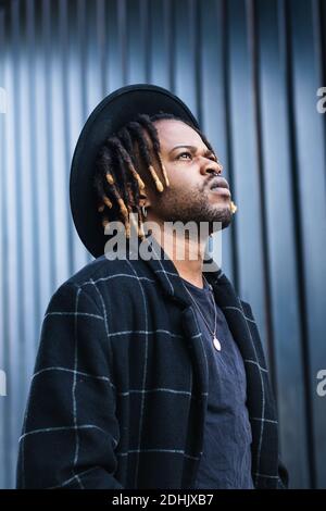 Homme ethnique barbu informel avec des dreadlocks et dans le chapeau regardant debout dans la rue Banque D'Images
