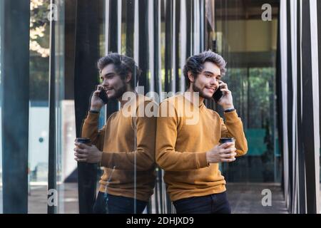 Jeune homme excité avec de longs cheveux bouclés debout sur la colline contre une vaste vallée spectaculaire et prendre le selfie sur mobile moderne téléphone Banque D'Images