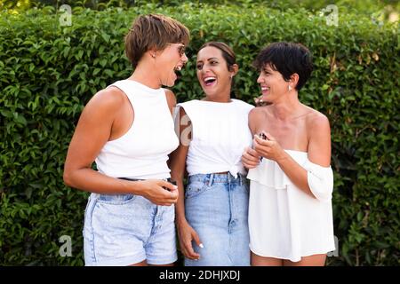 Groupe de femmes insouciantes se tenant ensemble et s'amusant pendant que vous êtes dans le parc de la ville et que vous riez à la blague Banque D'Images