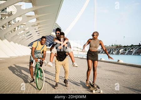 Compagnie joyeuse d'amis afro-américains à bord de long et à vélo près du couple de piggydorage tout en s'amusant et amusant en ville en été Banque D'Images