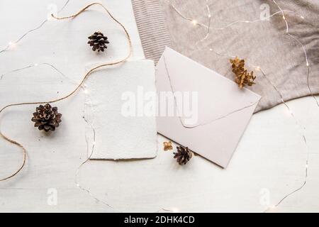 Concept de liste de souhaits de Noël. Maquette de lettre vierge sur papier artisanal. Enveloppe de lettre, cônes de pin, fil d'artisanat et bougie. Style décontracté. Plat Banque D'Images