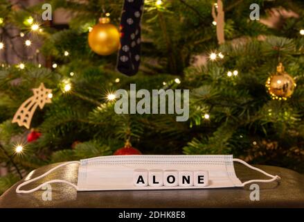 Symbole pour les personnes seules pendant la période de Noël 2020. Les dés forment le mot « seul » au-dessus d'un masque facial devant un arbre de Noël. Banque D'Images