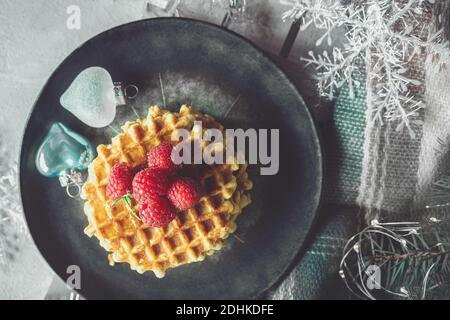 gaufres viennoises avec framboises et miel sur la table de noël avec branches d'arbre de noël et guirlandes de lumières en arrière-plan. vue du dessus . Banque D'Images