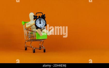 Symbole du temps de vente. Modèle en bois d'un homme dans un chariot avec réveil noir. Magnifique arrière-plan orange. Concept d'affaires et de vente, copie SPAC Banque D'Images