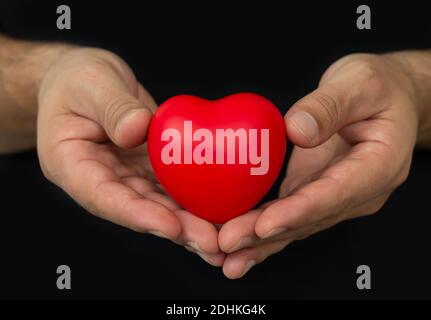 Homme qui hose le cœur rouge sur fond sombre. Concept de personnes, de relations, de santé et d'amour Banque D'Images