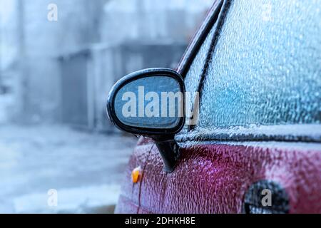 Le rétroviseur extérieur de la voiture s'est gelé après une pluie verglaçante. Un temps anormal, une pluie verglaçante couvrait la voiture rouge de la croûte de glace. Technique de mise au point douce Banque D'Images