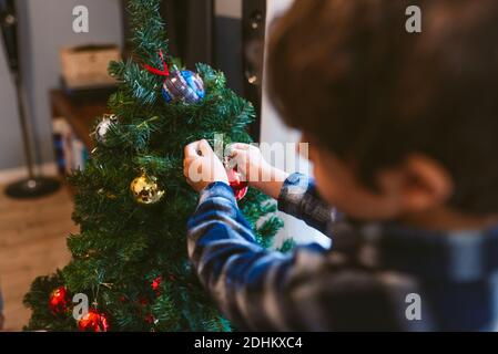 noël en famille à la maison. mignon petit enfant garçon décorant arbre de noël à l'intérieur pendant la saison des vacances. en hiver avec lumière naturelle chaude et douce Banque D'Images