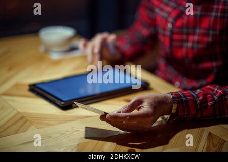 Une femme mûre fait des achats en ligne en utilisant un ordinateur tablette dans un café. Une femme plus âgée paie pour le paiement en ligne par carte de crédit. Moderne senior utilise plastique c Banque D'Images