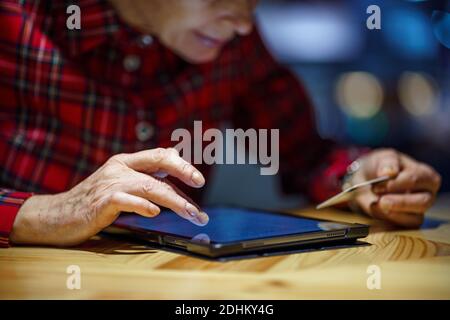 Une femme mûre fait des achats en ligne en utilisant un ordinateur tablette dans un café. Une femme plus âgée paie pour le paiement en ligne par carte de crédit. Moderne senior utilise plastique c Banque D'Images