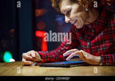 Une femme mûre fait des achats en ligne en utilisant un ordinateur tablette dans un café. Une femme plus âgée paie pour le paiement en ligne par carte de crédit. Moderne senior utilise plastique c Banque D'Images