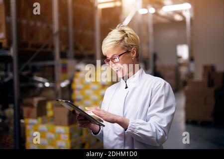 Une jeune femme joyeuse tient une tablette et sourit dans la zone de chargement de l'usine. Banque D'Images