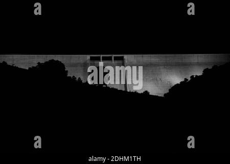 Barrage Enciso illuminé la nuit avec une silhouette de montagnes et de chênes devant. Photo en noir et blanc. Banque D'Images