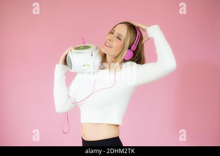 J'aime écouter de la musique avec un casque. Portrait d'une belle femme blonde sur fond rose écoutant de la musique avec un casque. Elle se tient à droite Banque D'Images