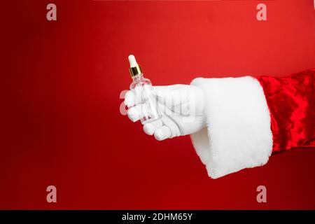 Maquette de bouteille en verre avec main de Père Noël. Pipette cosmétique sur fond rouge Banque D'Images