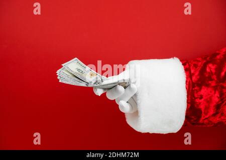 Main du Père Noël tenant de l'argent sur fond rouge. Main avec de l'argent. Banque D'Images