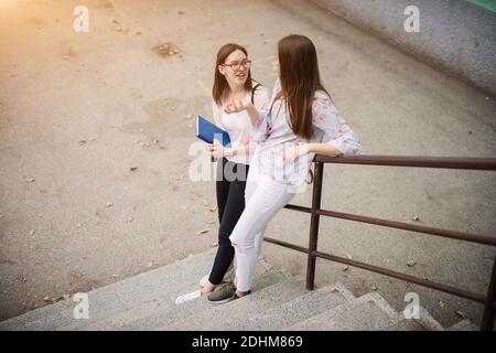 Deux charmantes filles d'école secondaire debout sur les escaliers se penchant contre la clôture et ayant une conversation. Banque D'Images