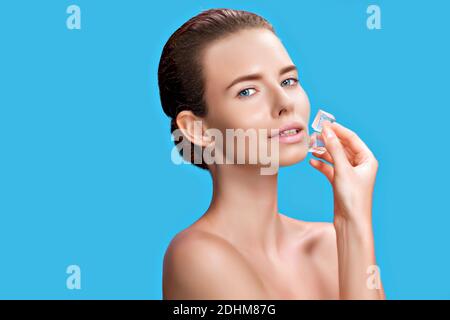 Belle femme appliquant le traitement de cube de glace sur fond bleu. Banque D'Images