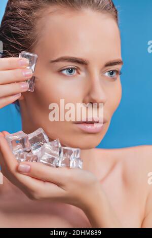 Belle femme appliquant le traitement de cube de glace sur fond bleu. Banque D'Images