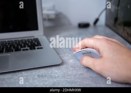 En tenant une souris d'ordinateur blanche grise près d'un ordinateur portable un bureau à main masculine Banque D'Images