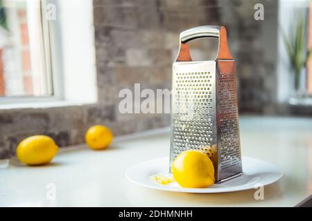 Zeste de citron et de citron avec râpe en métal sur la plaque blanche sur la table de cuisine. Couleurs tendance jaune et gris de l'année 2021. Sélectif Banque D'Images