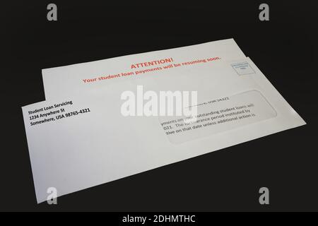 Un avis de reprise des paiements de prêt étudiant dans une enveloppe sur un bureau noir, à gauche inclinée. Banque D'Images