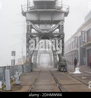 Les piétons traversent le brouillard en passant par le musée M Shed et les grues historiques sur le quai flottant de Bristol. Banque D'Images