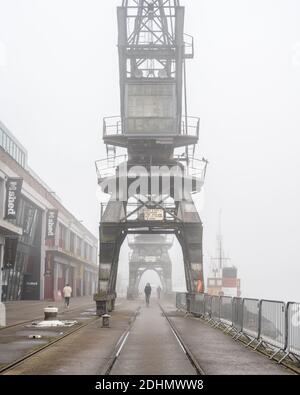 Les piétons traversent le brouillard en passant par le musée M Shed et les grues historiques sur le quai flottant de Bristol. Banque D'Images