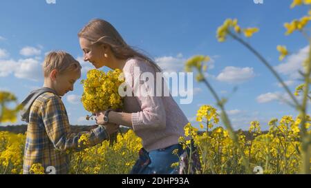 Un fils affectueux donne à sa mère des fleurs de colza dans un champ de colza. Banque D'Images