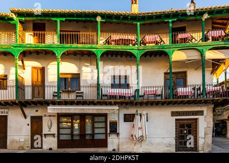 Balcons en bois vert flanqués d'arcades avec restaurants avec cousine espagnole traditionnelle sur la place médiévale principale de Chinchón, Espagne. Banque D'Images