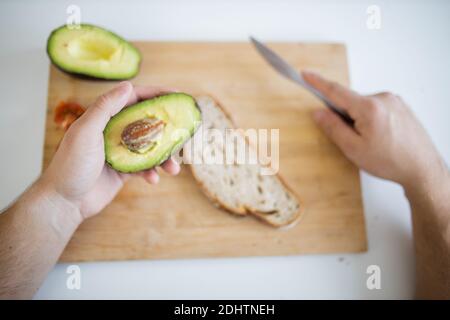 Main mâle tenant l'avocat tranché au-dessus d'une planche à découper Banque D'Images