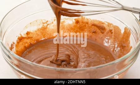 Gros plan de la pâte à muffins au chocolat dans un bol en verre, en mélangeant les ingrédients à l'aide d'un fouet Banque D'Images