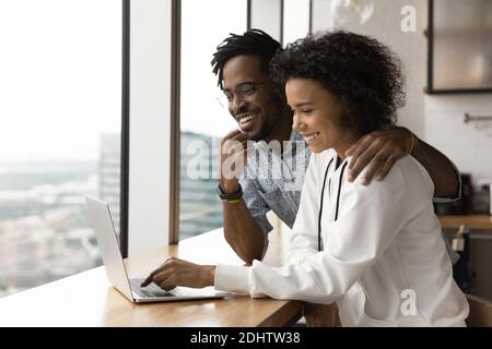 Un couple biracial heureux utilise un ordinateur portable à la maison ensemble Banque D'Images