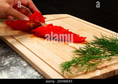 le chef cuisinier de fille coupe des tomates fraîches parfumées pour faire de la pizza italienne sur une cuisine en bois Banque D'Images