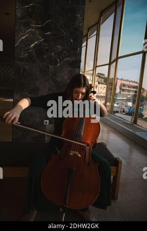 Adolescente avec violoncelle, posant dans un hall. Banque D'Images