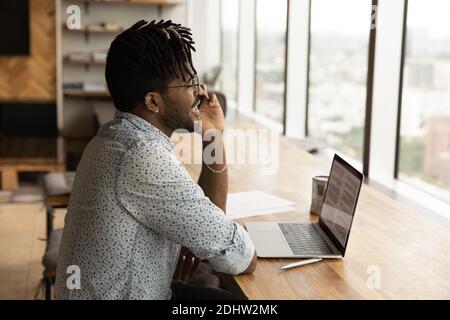 Un homme biracial souriant travaille sur un ordinateur portable et parle sur une cellule Banque D'Images
