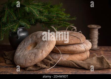 Quatre pains ronds avec trou au milieu, certains d'entre eux sont attachés par une corde de jute. Pains à tamis de seigle à l'ancienne. Sur une table brun rétro, avec un vase W Banque D'Images