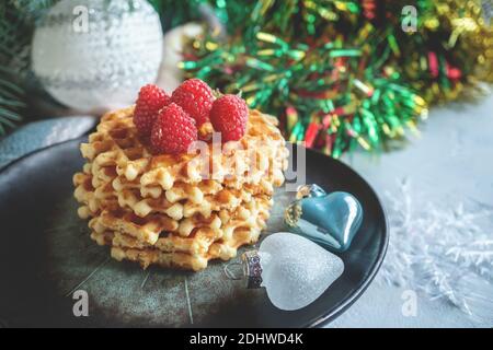 gaufres viennoises avec framboises et miel sur la table de noël avec branches d'arbre de noël et guirlandes de lumières en arrière-plan. Banque D'Images