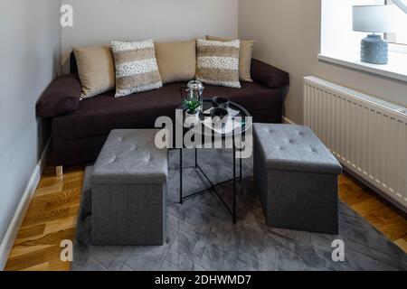 Intérieur moderne du petit salon. Murs gris. Canapé confortable avec coussins. Table basse noire. Tabourets rembourrés doux. Banque D'Images