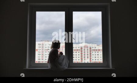 Enfant solitaire fille assise sur la fenêtre à la fenêtre dans les appartements. Banque D'Images