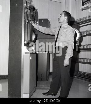 Années 1960, technicien de studio historique et masculin qui vérifie les bobines de film sur une cassette RCA dans une nouvelle installation de télévision, Arabie Saoudite. Banque D'Images