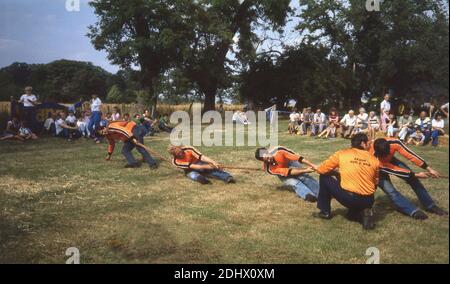 Dans les années 1970, des concurrents masculins historiques en dehors du terrain participent à un concours de tir à la corde, Angleterre Royaume-Uni, avec un entraîneur à côté d'eux exigeant plus d'effort. Dans un événement de Tug of War, les membres de deux équipes doivent tirer sur une corde et l'amener à une certaine distance vers eux contre la force de la traction des oppositions. Le remorqueur de la guerre a une longue histoire comme activité amusante lors d'événements en plein air et comme sport de compétition, comme il faisait partie du programme olympique d'été dans les années 1900 à 1920. La British Tug of War Association a été créée en 1958. Banque D'Images