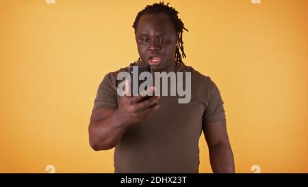 Un homme noir afro-américain choqué regardant l'écran de son téléphone. Message texte inattendu ou mauvaises nouvelles. Photo de haute qualité Banque D'Images